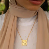 A close-up of a person wearing a Silver gold pendant necklace with Arabic calligraphy in kufi font style.