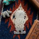 Hand-engraved silver Handala pendant displayed on a blue and red woven textile next to a raw turquoise stone.